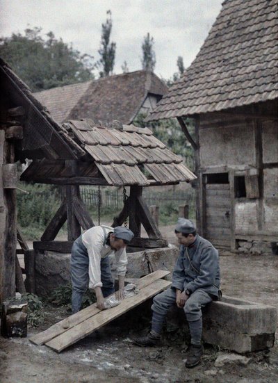 Two French soldiers taking care of their laundry using boards set up on the trough of a fountain near a farm house in the town of Gildwiller, Department Haut-Rhin, Alsace, France, June 21, 1917 by Paul Castelnau